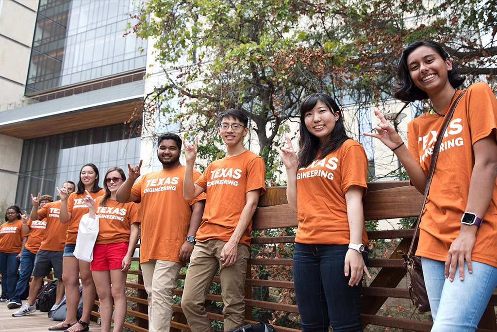 UT students wearing Texas engineering t-shirts standing on bridge doing hook 'em horns hand sign