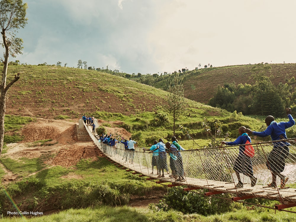 Children cross a rope footbridge over a valley.