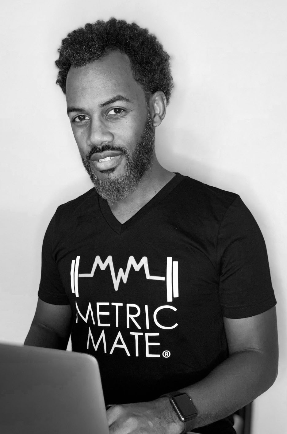 Ecleamus Ricks typing on computer wearing a Metric Mate t-shirt
