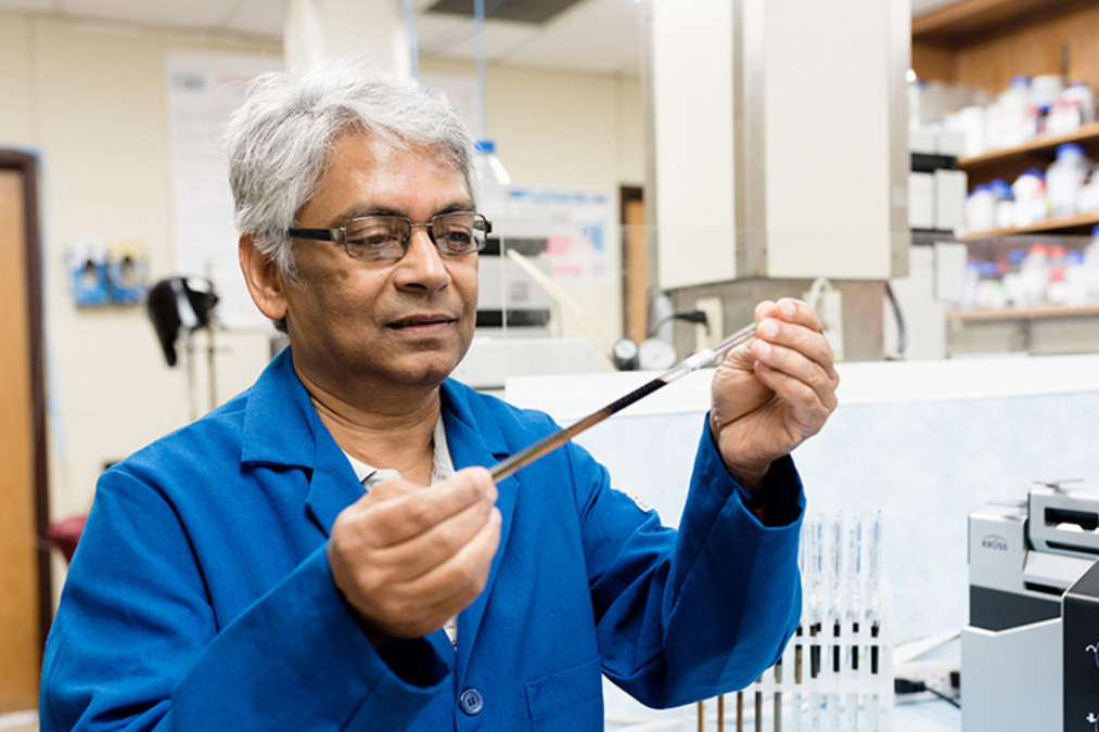 Kishore Mohanty in his lab, inspecting and holding a vial of oil
