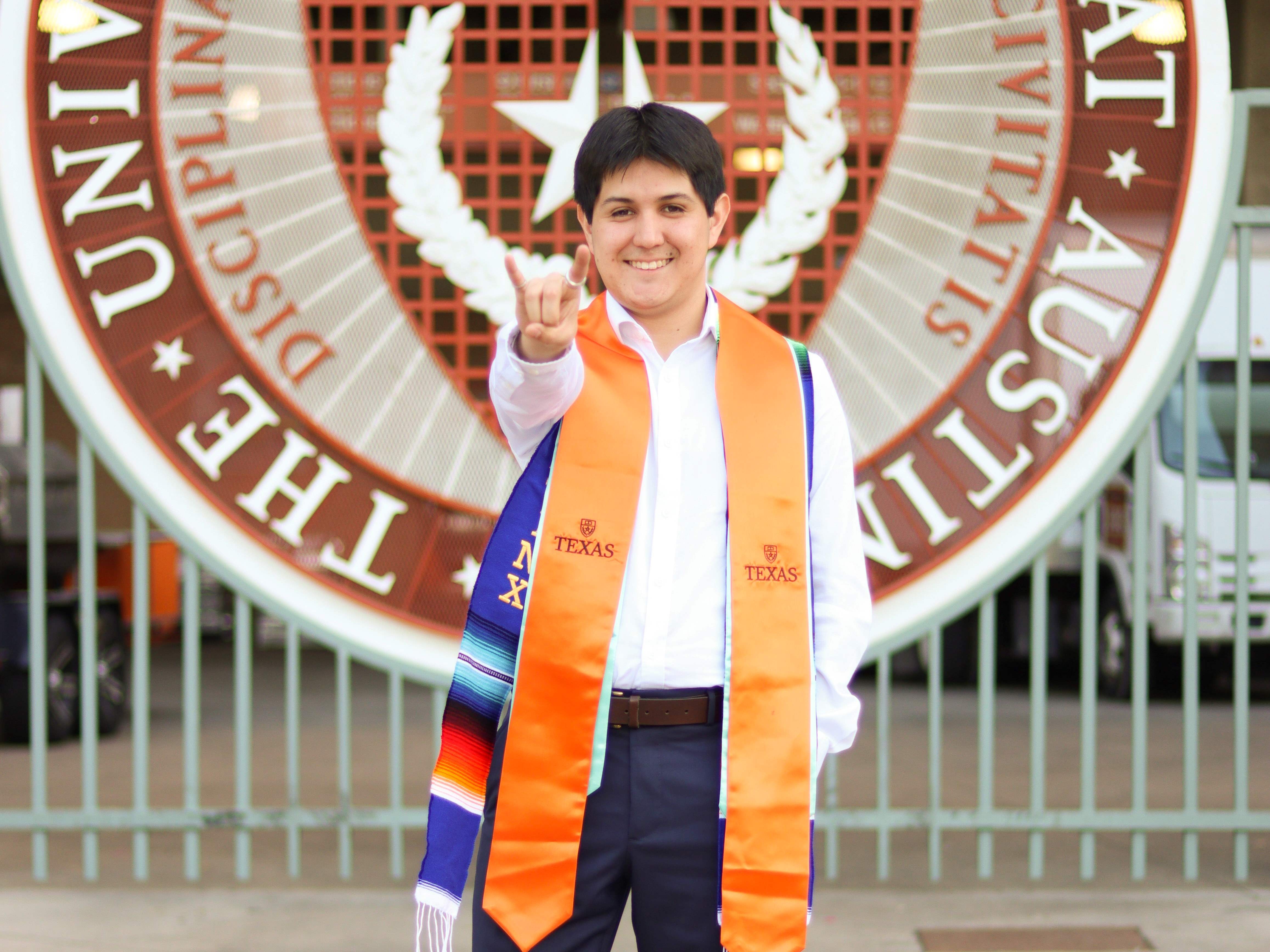 Texas engineer Jan Carlos Rubio wearing UT Austin graduation regalia and doing hook 'em horns hand sign